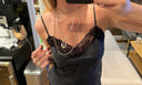 A woman in a black lace camisole takes a selfie, showcasing layered silver necklaces, including the striking Kathl-Gross T-CROSS NECKLACE. Her nails are painted dark, and the background features a kitchen counter and a beige sofa—an elegant touch to her look with this traditional cross jewelry from Kathl-Gross.